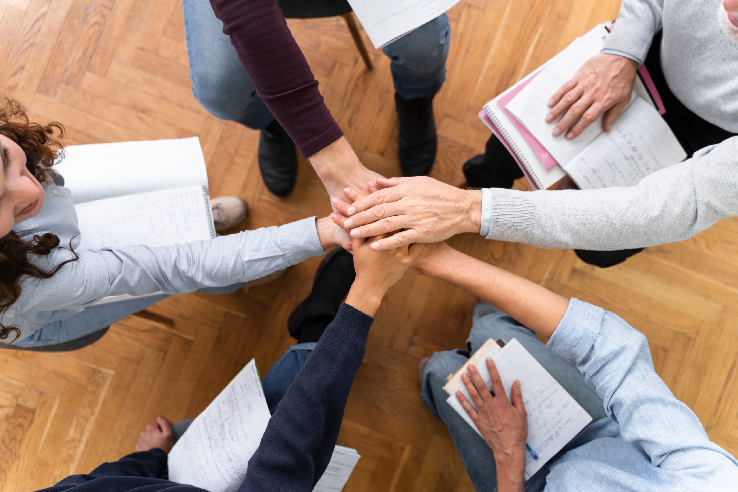 Cuatro personas uniendo sus manos sobre documentos y carpetas, simbolizando colaboración y acuerdo para acceder al aval del 20% para comprar vivienda.
